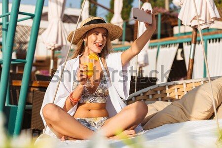 Caucasian woman 20s in straw hat smiling and taking selfie on mo Stock photo © deandrobot
