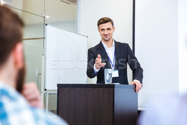 Smiling businessman standing at tribune in conference hall  Stock photo © deandrobot