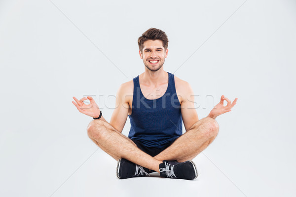Happy young sportsman sitting in lotus pose and smiling Stock photo © deandrobot