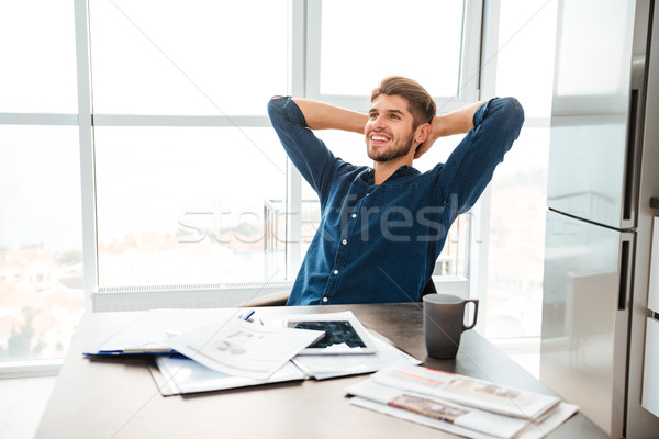 Cheerful young man sitting near table and stretching at home Stock photo © deandrobot