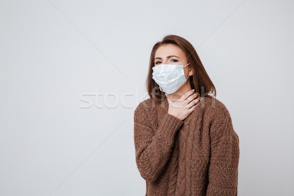 Woman in sweater and medical mask holding her neck Stock photo © deandrobot
