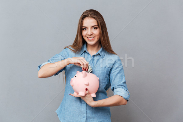 Stock photo: Woman putting money in piggy bank