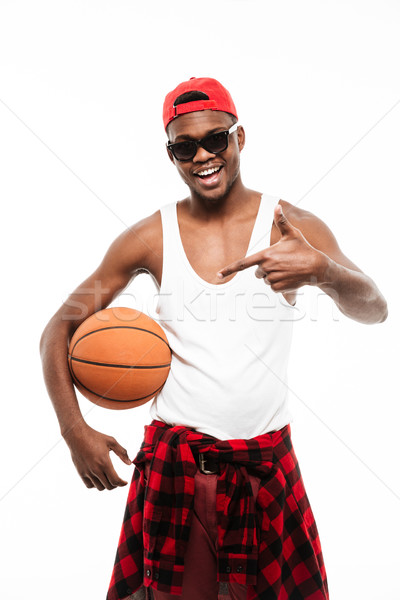 Happy african young man holding basketball ball and pointing away Stock photo © deandrobot