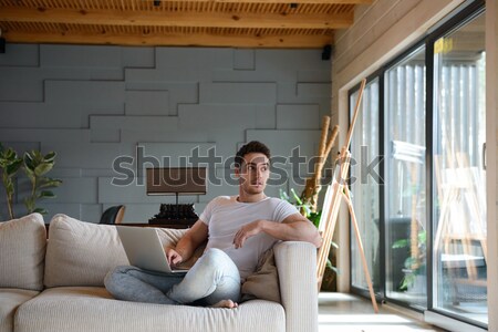 Young man using laptop while sitting in living room Stock photo © deandrobot