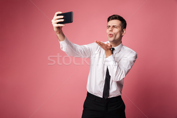 Handsome young businessman make selfie by mobile phone blowing kisses. Stock photo © deandrobot