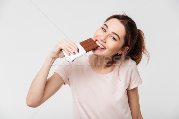 Portrait of a smiling pretty girl biting chocolate bar Stock photo © deandrobot