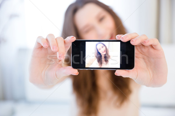 Playful positive woman winking and taking selfie with smartphone  Stock photo © deandrobot