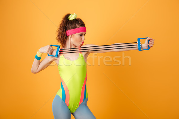 Serious focused young fitness woman standing and training with expander Stock photo © deandrobot