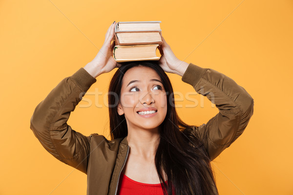 Happy asian woman in jacket holding books on head Stock photo © deandrobot