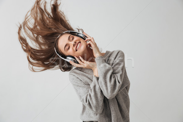 Cheerful brunette woman in sweater and headphones listening music Stock photo © deandrobot