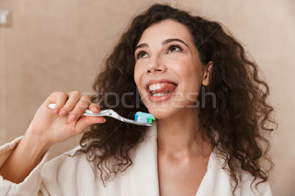 Beautiful young cute woman in bathroom brushing cleaning her teeth. Stock photo © deandrobot