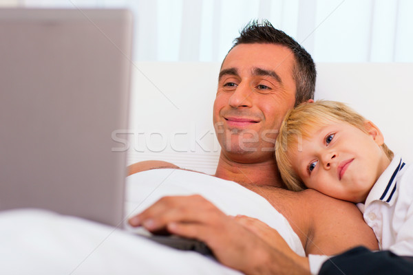 Father and son in bed, using laptop together Stock photo © deandrobot