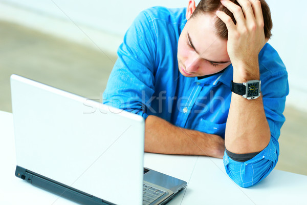 Young thoughtful businessman in blue shirt sitting at the table with laptop in office Stock photo © deandrobot