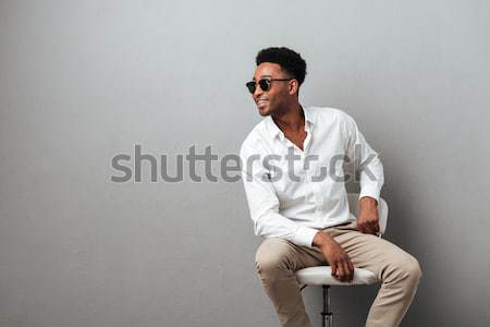 Fashion portrait of attractive young man sitting and holding sunglasses Stock photo © deandrobot