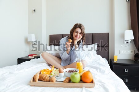 Stock photo: Woman sitting on bed and pointing at tray with breakfast