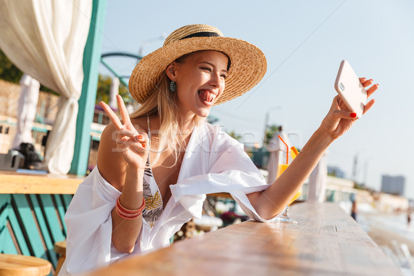 Photo of cheerful blonde woman 20s in straw hat laughing and tak Stock photo © deandrobot