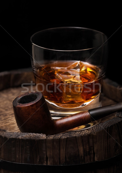 Glass of whiskey with ice cubes and vintage smoking pipe on top of wooden barrel. Cognac brandy drin Stock photo © DenisMArt