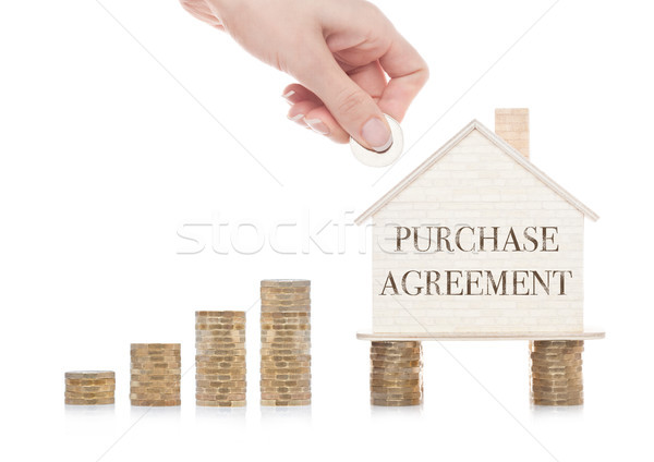 Stock photo: Wooden house model standing on coins and hand