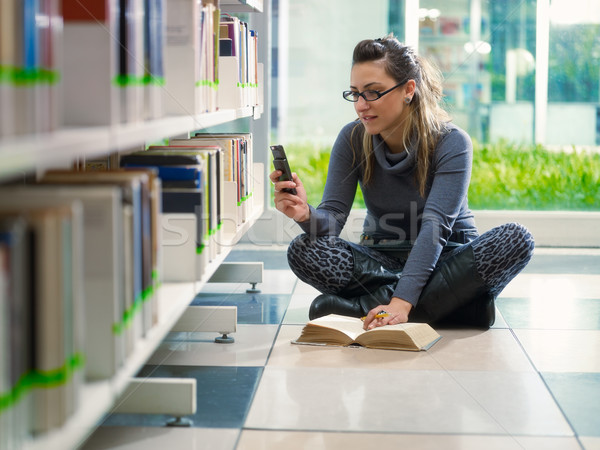 Stock photo: girl text messaging with phone in library