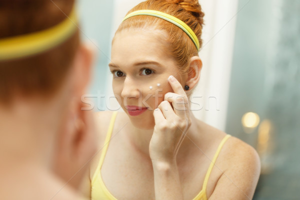 Young Woman Applies Anti-Aging Cream Looking At Mirror Stock photo © diego_cervo