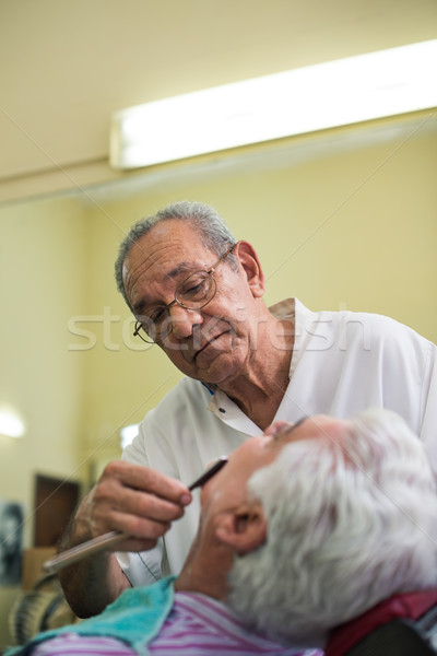 Elderly barber with razor shaving client in barber shop Stock photo © diego_cervo