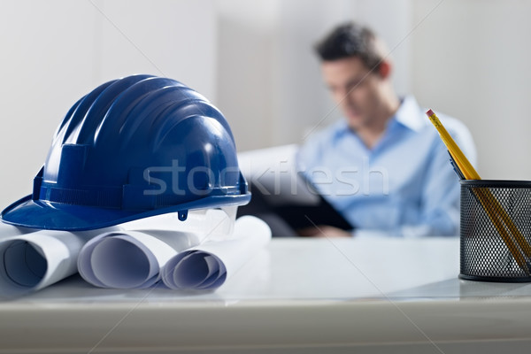 Stock photo: hardhat and blueprint on desk, with architect in background