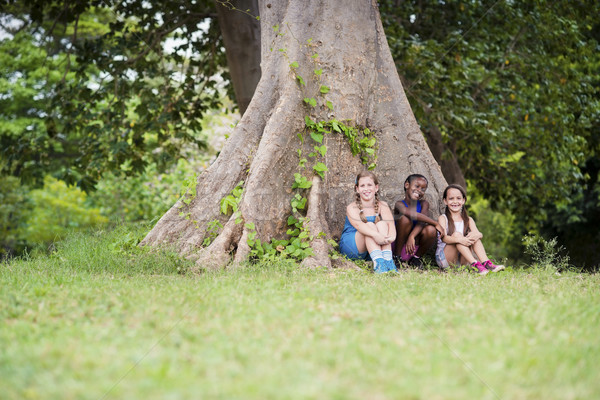 Stock photo: Three happy female friends sitting near big tree