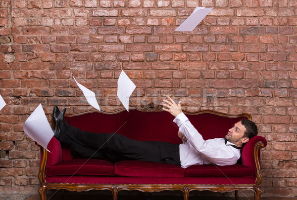 Stock photo: Businessman lying on a settee with flying papers