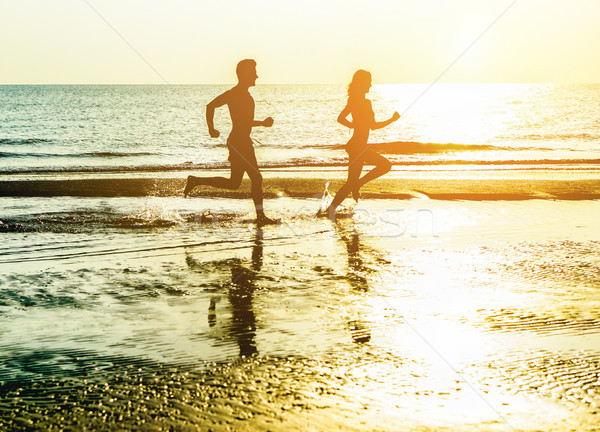 Silhouette of young happy couple running on seashore splashing w Stock photo © DisobeyArt