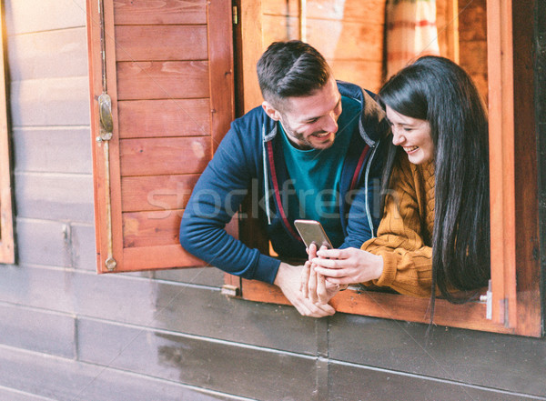 Happy couple having fun with smartphone inside camping wood hous Stock photo © DisobeyArt