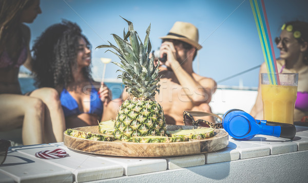 Happy friends having fun and eating pineapple fruit at boat part Stock photo © DisobeyArt