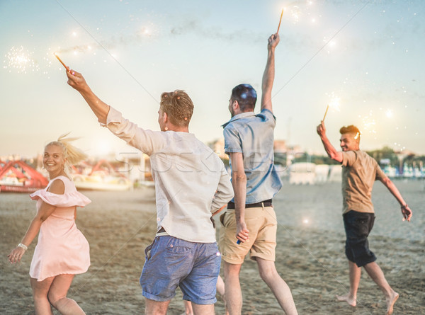 Group of happy friends running on the beach with fireworks spark Stock photo © DisobeyArt