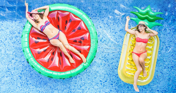 Happy girls floating with tropical fruit lilos inside swimming p Stock photo © DisobeyArt