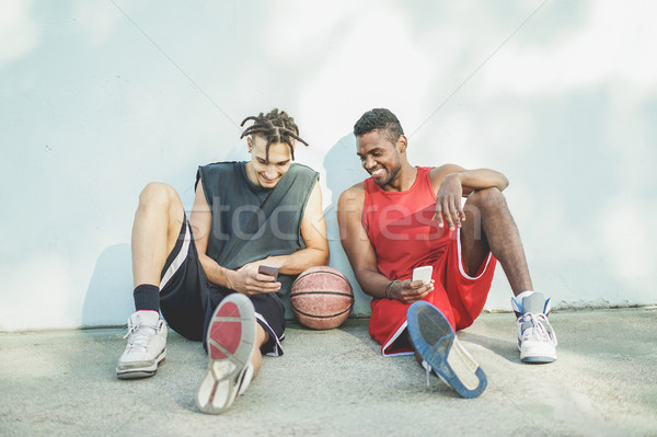 Young cheerful basket ball players having fun with smart phone o Stock photo © DisobeyArt