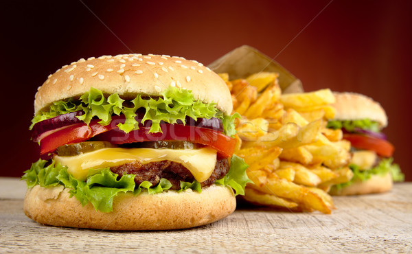Cheeseburger and french fries on red spotlight on wooden table Stock photo © dla4