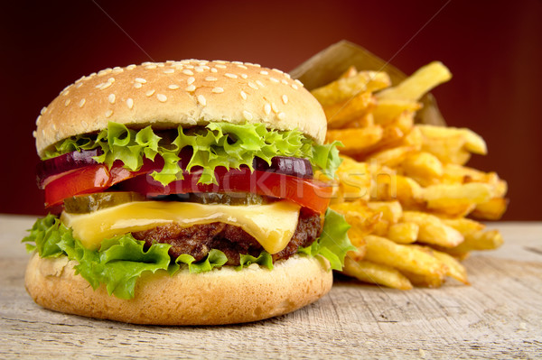 Stock photo: Cheeseburger and french fries on red spotlight on wooden table