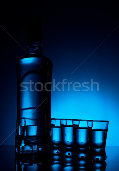 Bottle of vodka with many glasses lit with blue backlight Stock photo © dla4