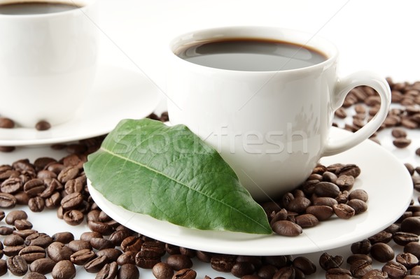 Scattered coffee beans with cups of coffee and leaf Stock photo © dla4