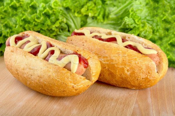 Hotdogs with mustard and ketchup with lettuce in the background on wooden desk Stock photo © dla4