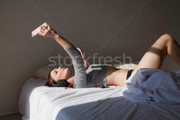 a girl takes photo on a smartphone on the bed with headphones Stock photo © dmitriisimakov