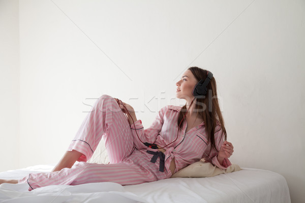 brunette in pink Pajamas listening to music with headphones on the bed Stock photo © dmitriisimakov