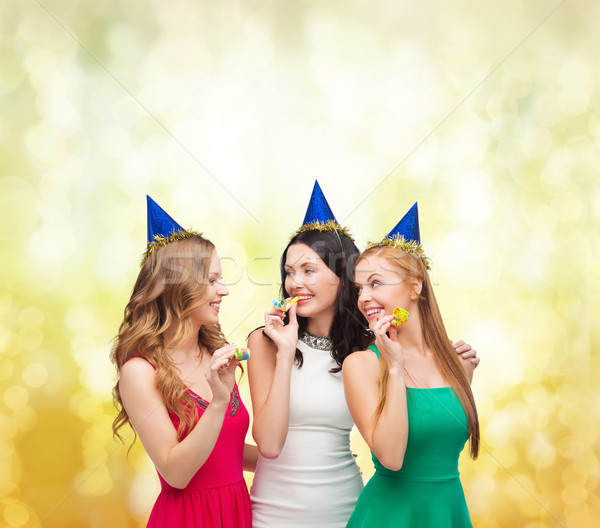 three smiling women in hats blowing favor horns Stock photo © dolgachov