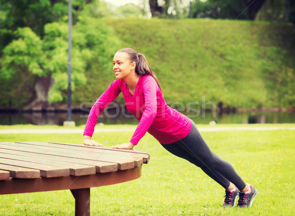 smiling woman doing push-ups on bench outdoors Stock photo © dolgachov