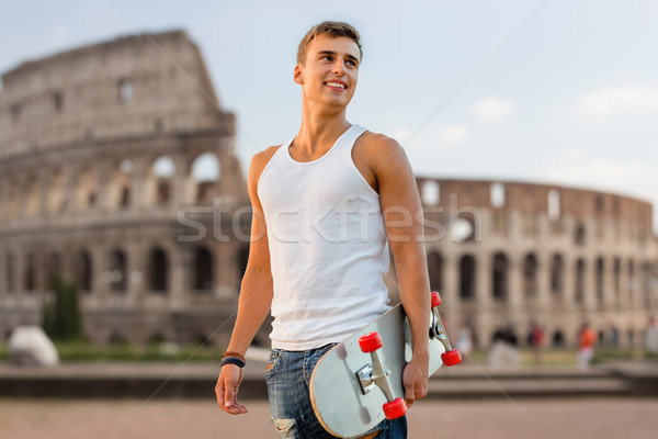 smiling teenage boy with skateboard over coliseum Stock photo © dolgachov