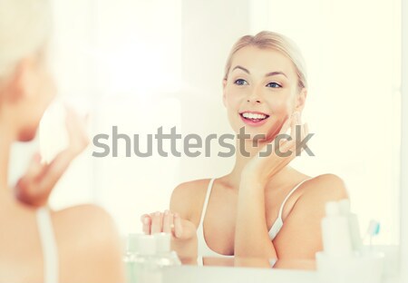 happy woman applying cream to face at bathroom Stock photo © dolgachov