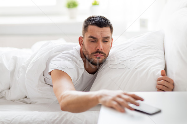 young man reaching for smartphone in bed Stock photo © dolgachov