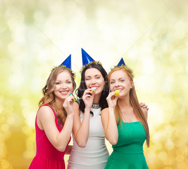 three smiling women in hats blowing favor horns Stock photo © dolgachov