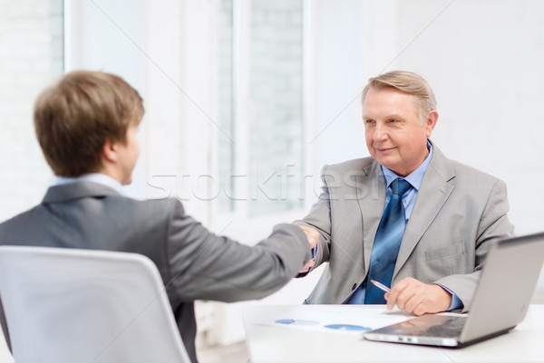 older man and young man shaking hands in office Stock photo © dolgachov