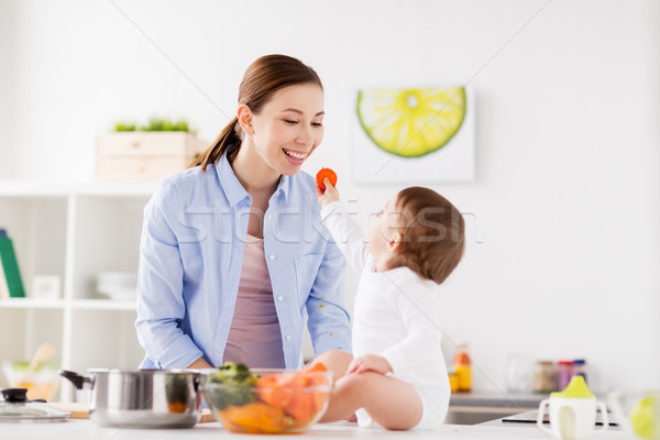 Stock photo: baby feeding mother with carrot at home kitchen