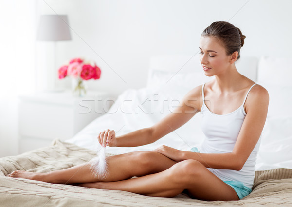 Stock photo: woman with feather touching bare legs on bed